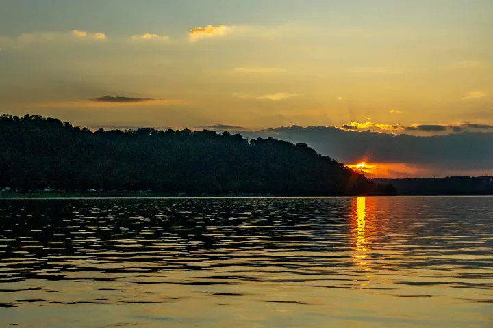 Sunset over a lake with orange sky and dark silhouetted hills.
